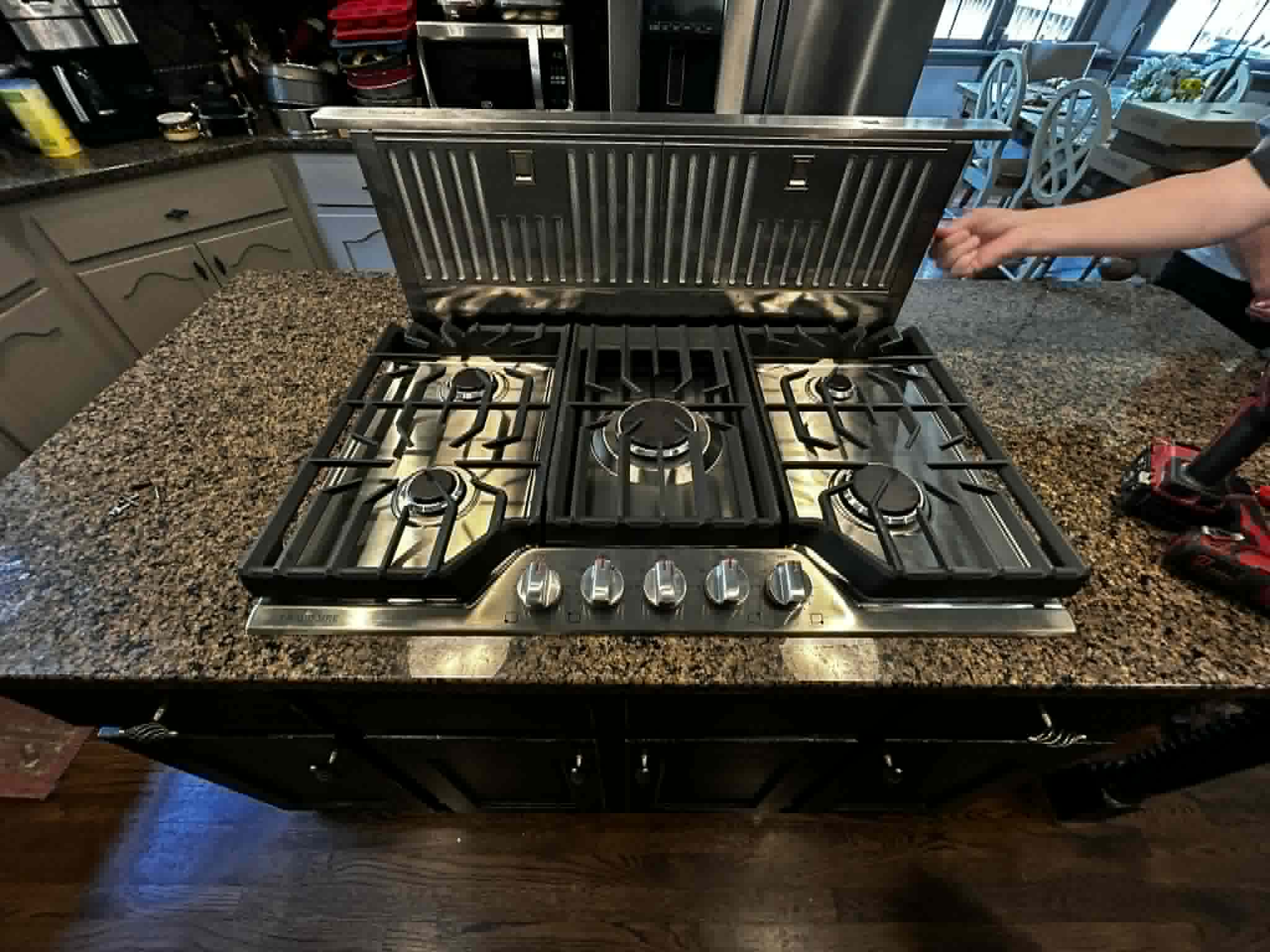 Stainless gas cooktop with downdraft vent installed in granite countertop.