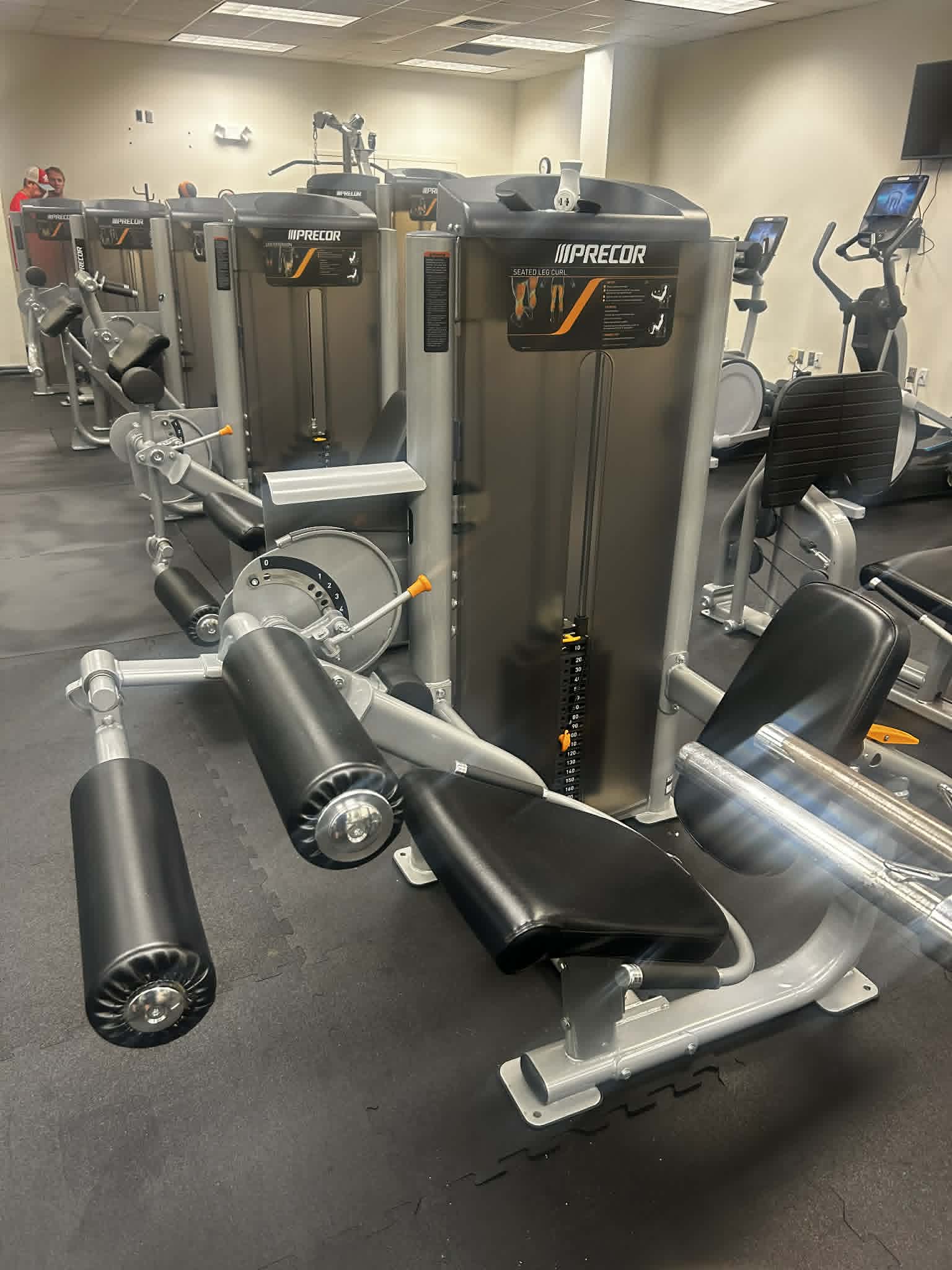 PRECOR seated leg curl machine in a clean, organized gym space.