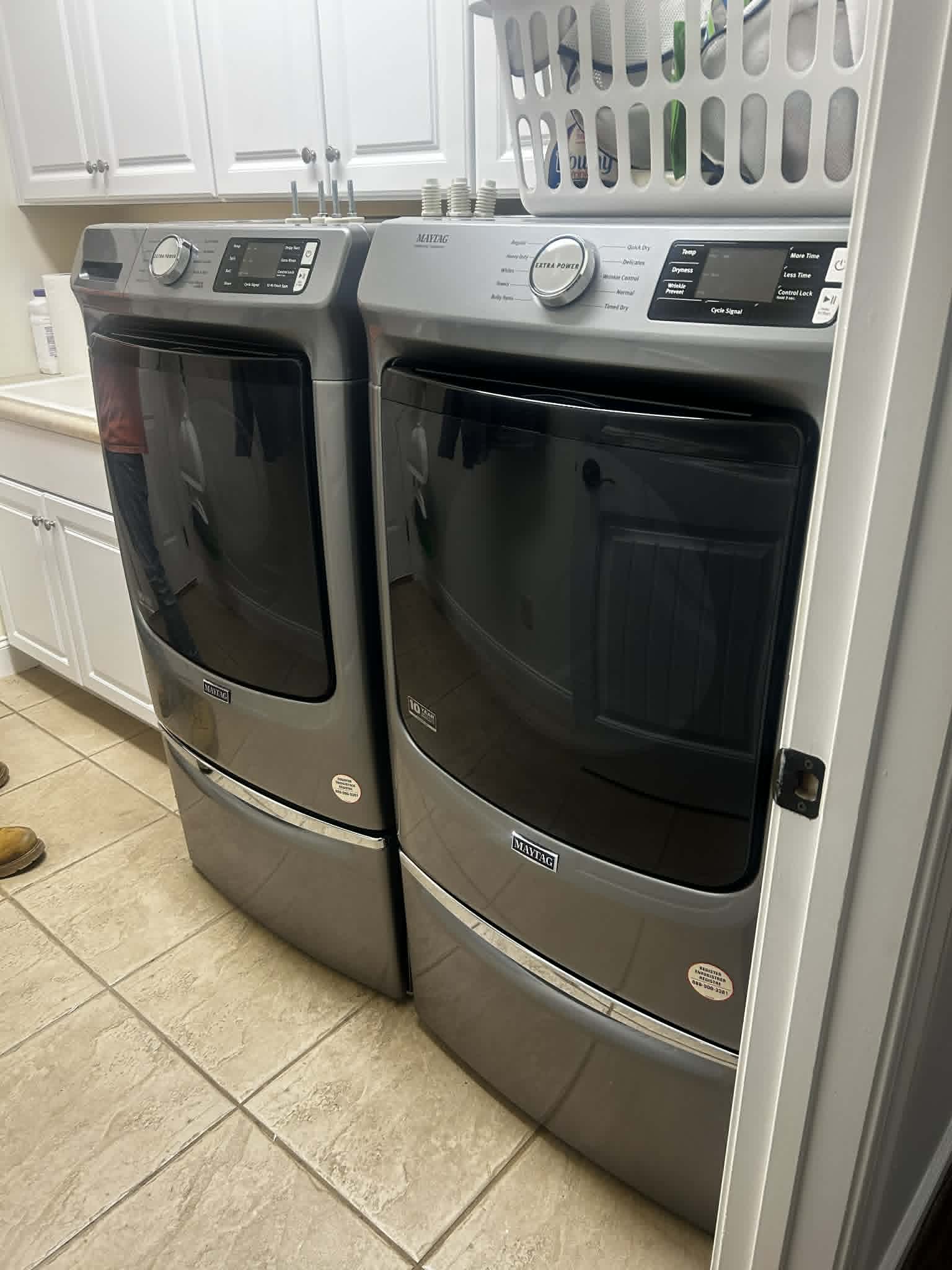 Modern laundry room with front-loading Maytag washer and dryer under white cabinetry.