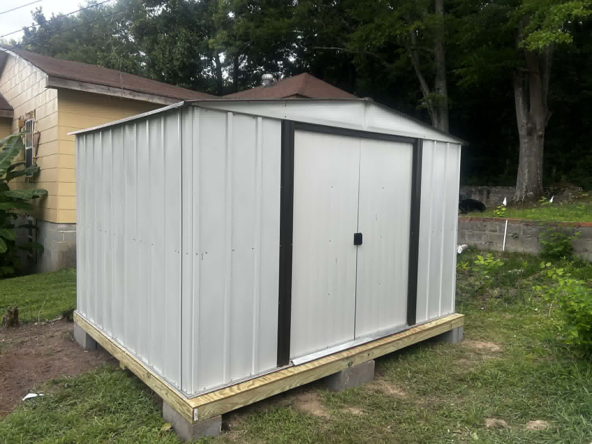 Elevated metal shed on wooden frame in grassy backyard.