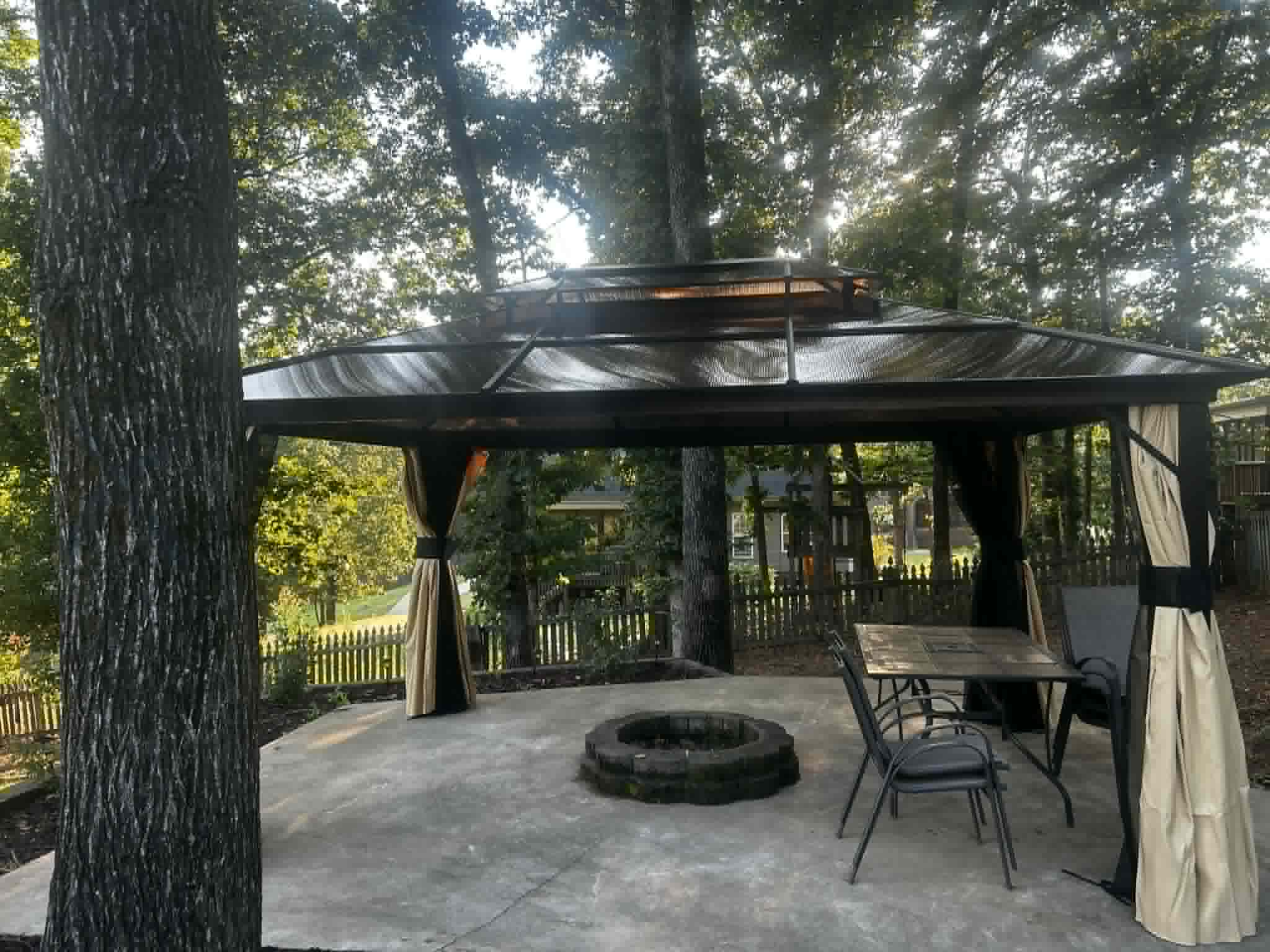 Large gazebo with curtains and stone fire pit on concrete patio.