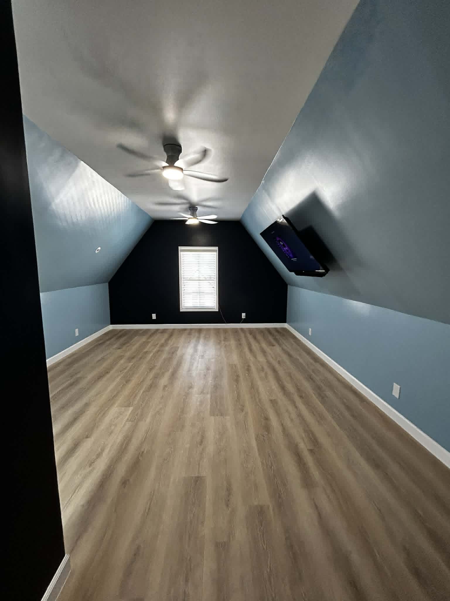 Finished attic room with slanted ceilings, ceiling fans, and wood flooring.