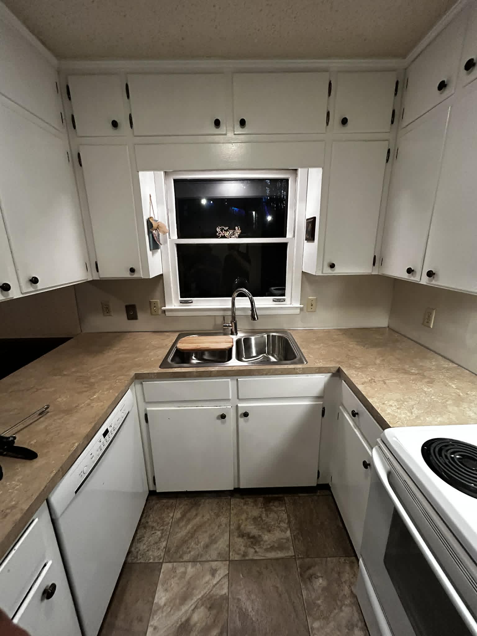 Compact kitchen with white cabinets, stainless sink, and tan countertops.