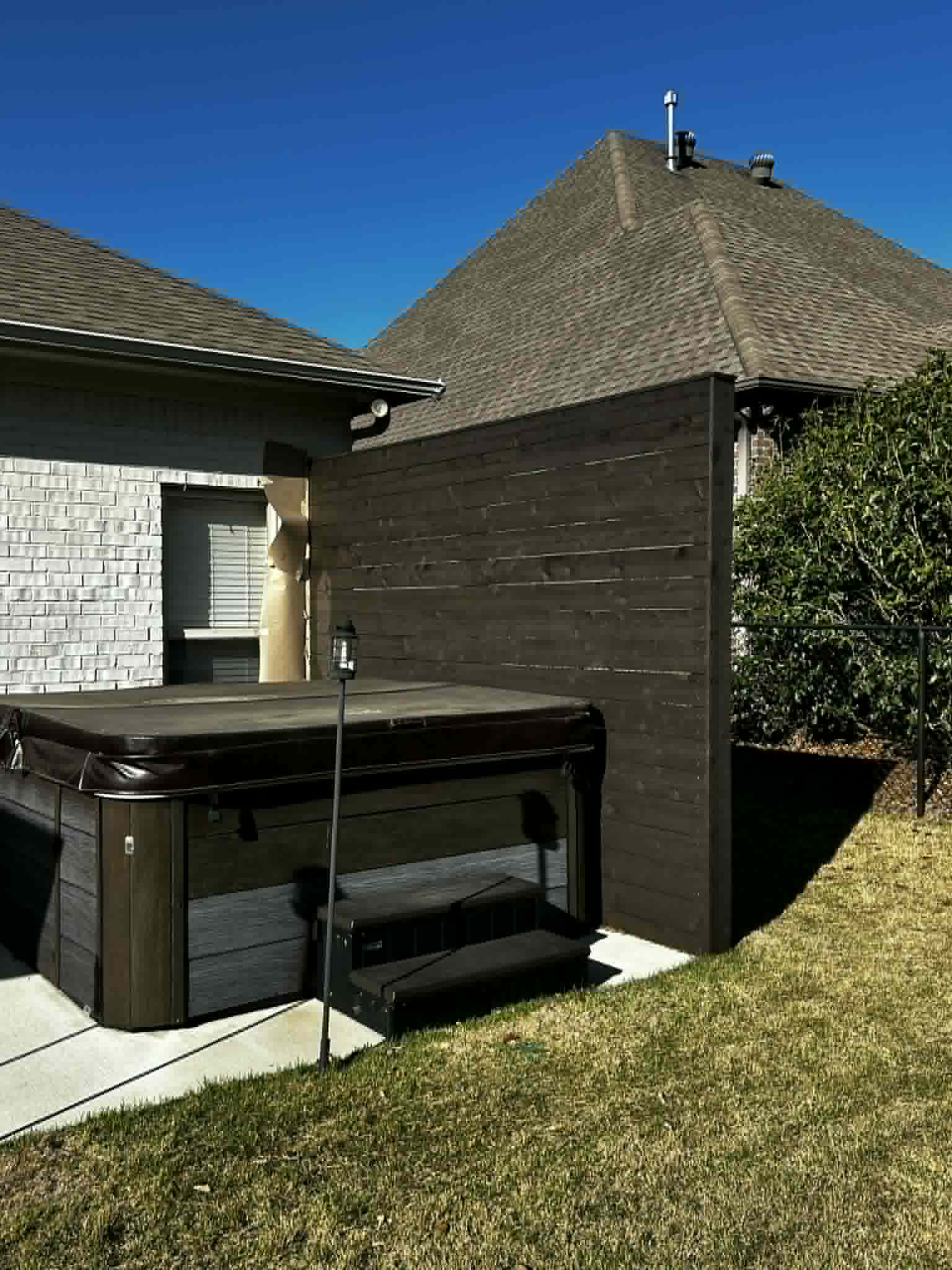 Hot tub on concrete pad with wooden privacy wall beside a brick home.